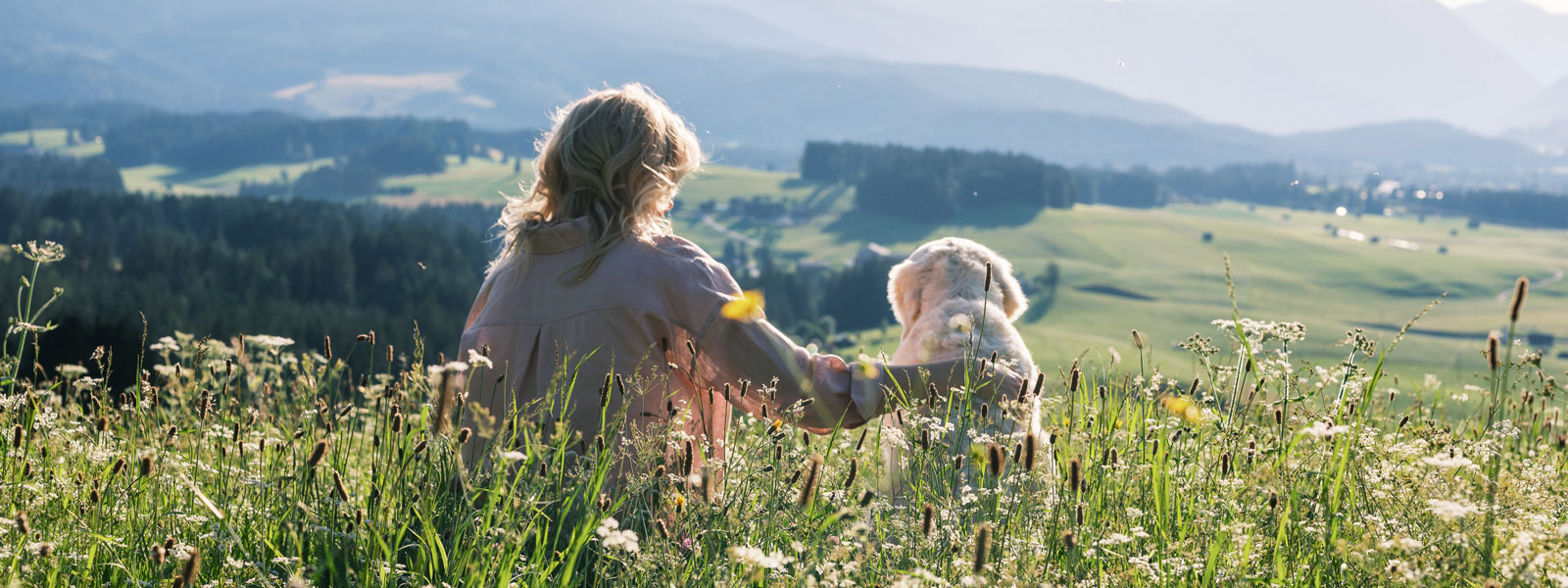 Katharina et Nala sont assises dans un pré et regardent, du haut d'une colline, la prairie et les bois en contrebas.