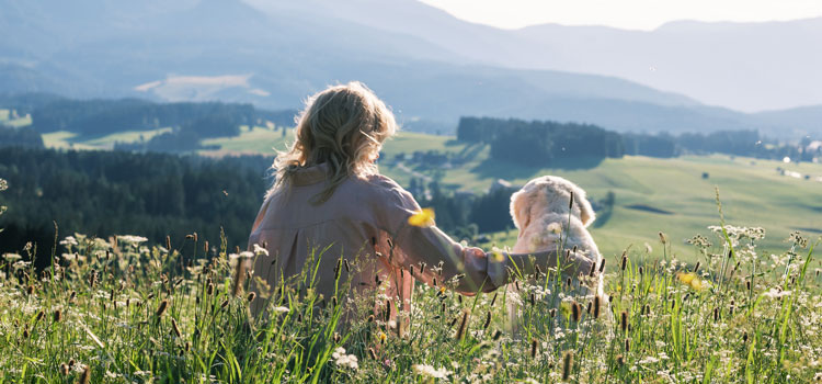 Katharina et Nala sont assises dans un pré et regardent, du haut d'une colline, la prairie et les bois en contrebas.